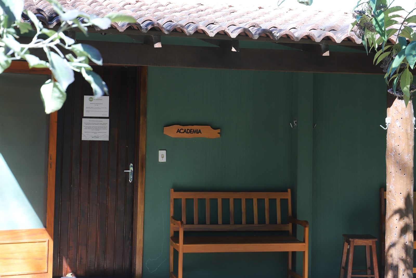 Fachada verde da academia, com a placa e o banco de madeira