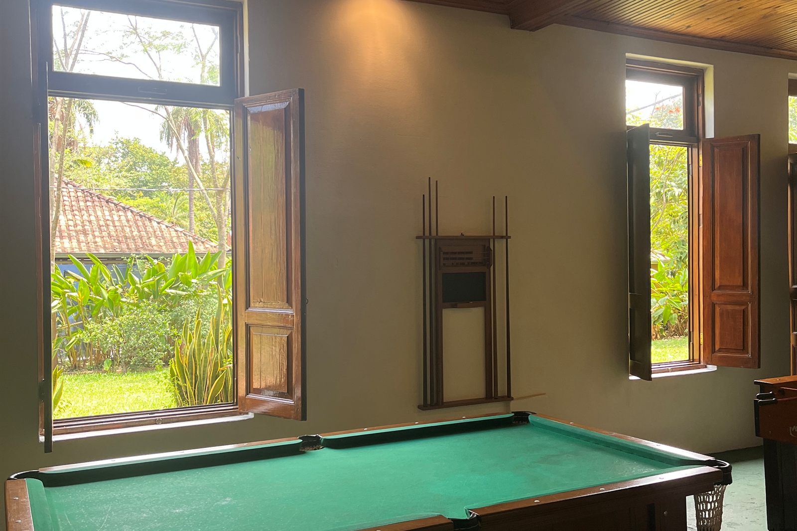 Mesa de sinuca diante das janelas abertas para o jardim